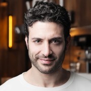 Smirking man with dark hair and five o'clock shadow